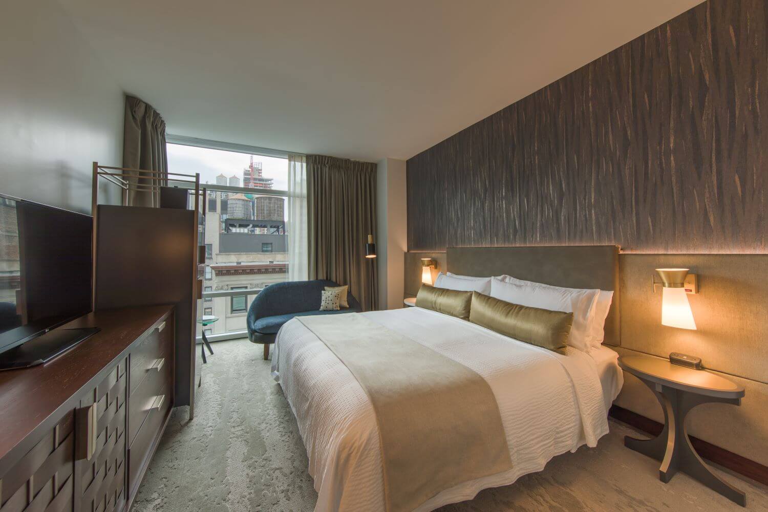 Guestroom with king bed, white linens, gold accents, and city views