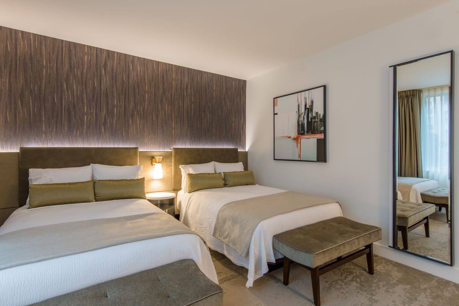 Guestroom with double beds, white linens, gold accents, and tufted benches